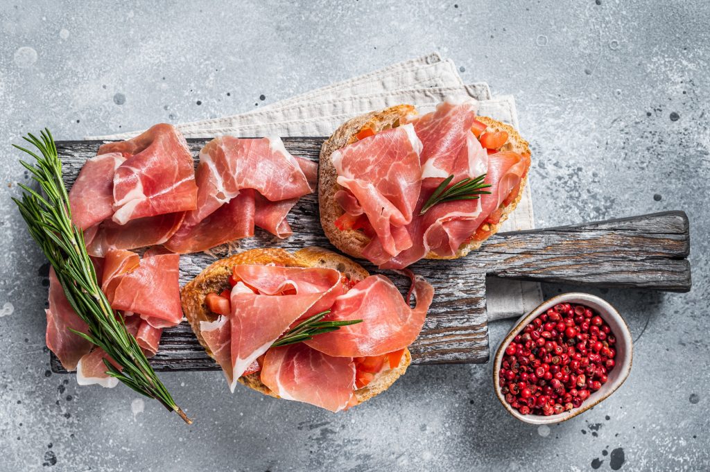 Spanish Tapas - Toast with tomatoes and cured Slices of jamon iberico ham on wooden board.