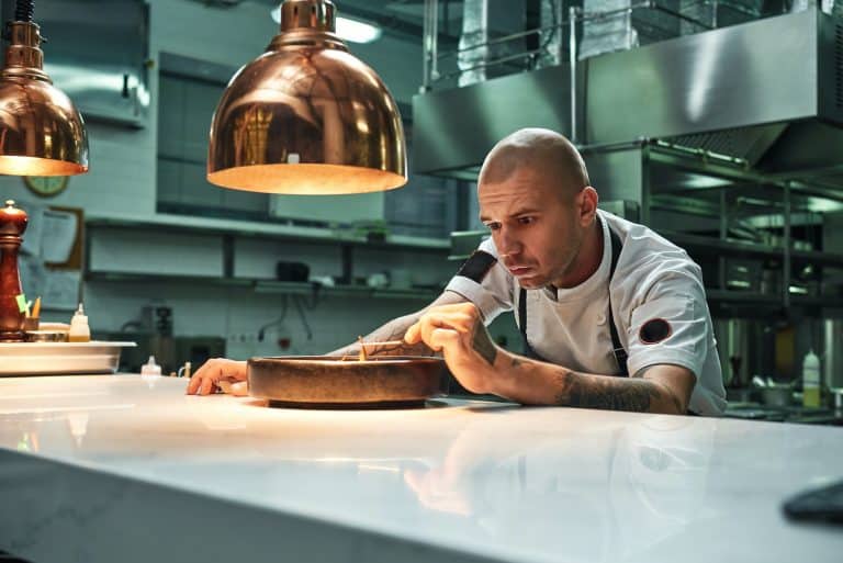 Trabajo delicado. Chef confiado decorando un delicioso pastel de chocolate mientras está de pie en un restaurante