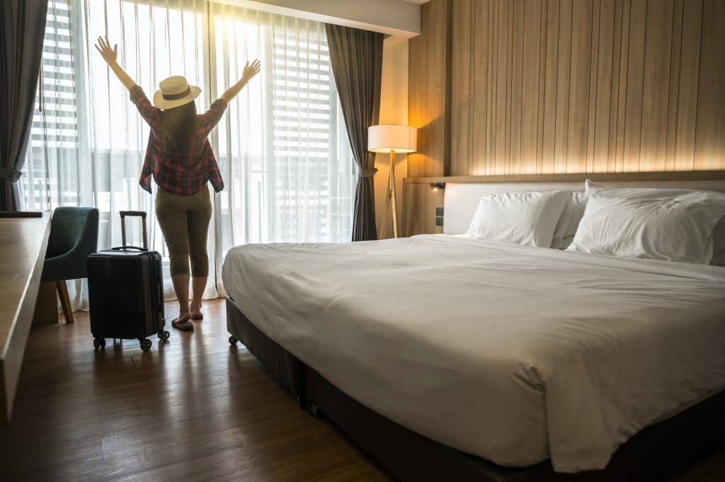 Felicidad mujer viajera asiática de pie con equipaje en el dormitorio del hotel o albergue