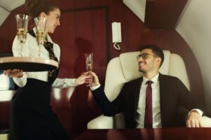Rich man travelling in his private jet, meeting stewardess who brings him glass of champagne