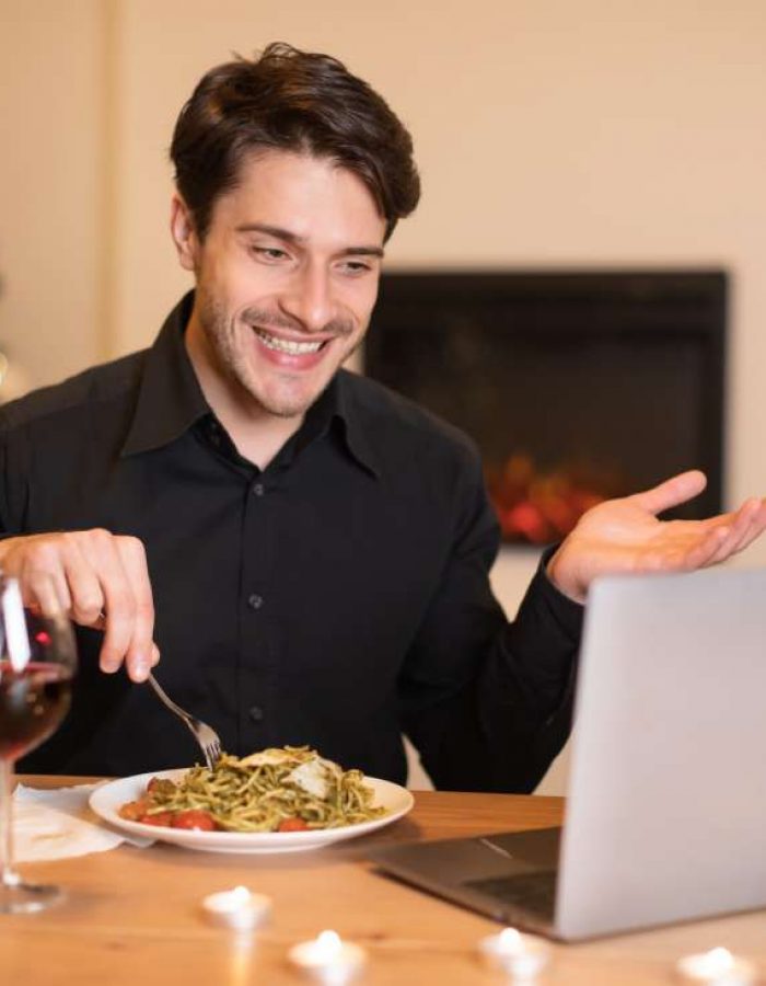 Hombre emocionado cenando durante una cita virtual en una laptop