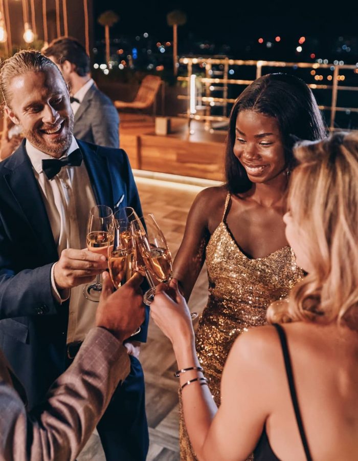 Grupo de personas en ropa formal comunicándose y sonriendo mientras pasan tiempo en una fiesta de lujo