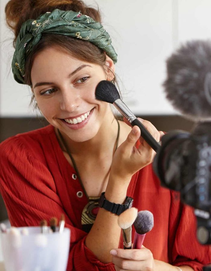 Retrato de una hermosa vloguera sonriente hace una revisión de video, usa un producto cosmético, registra el uso